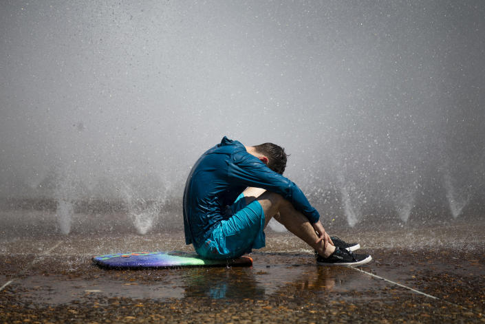 Sitting on the damp floor surrounded by sprinklers, a man in shorts and a long shirt soaks up the heat.