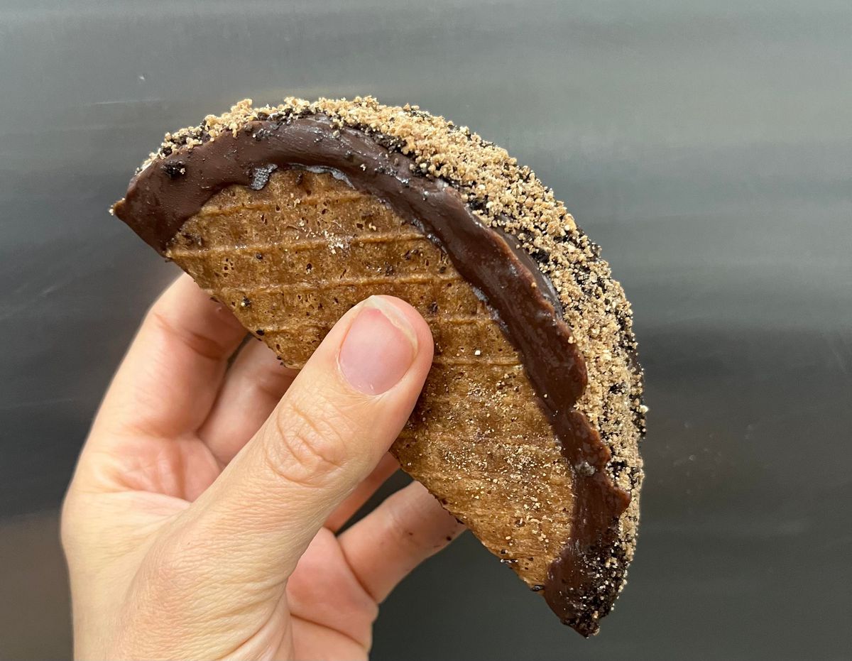 A hand holds a restaurant-made version of a Choco Taco dipped in chocolate and rolled in breadcrumbs.