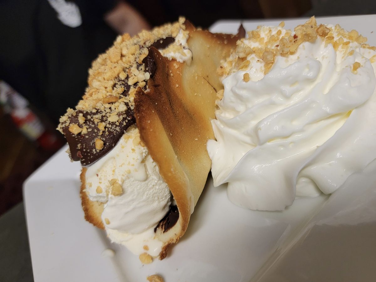 Scoops of vanilla, chocolate and crushed walnut ice cream are in a thin, cookie-like taco shell with a side of nutty whipped cream.