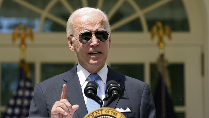 President Biden in front of the presidential seal, with two American flags with eagle finials behind him.