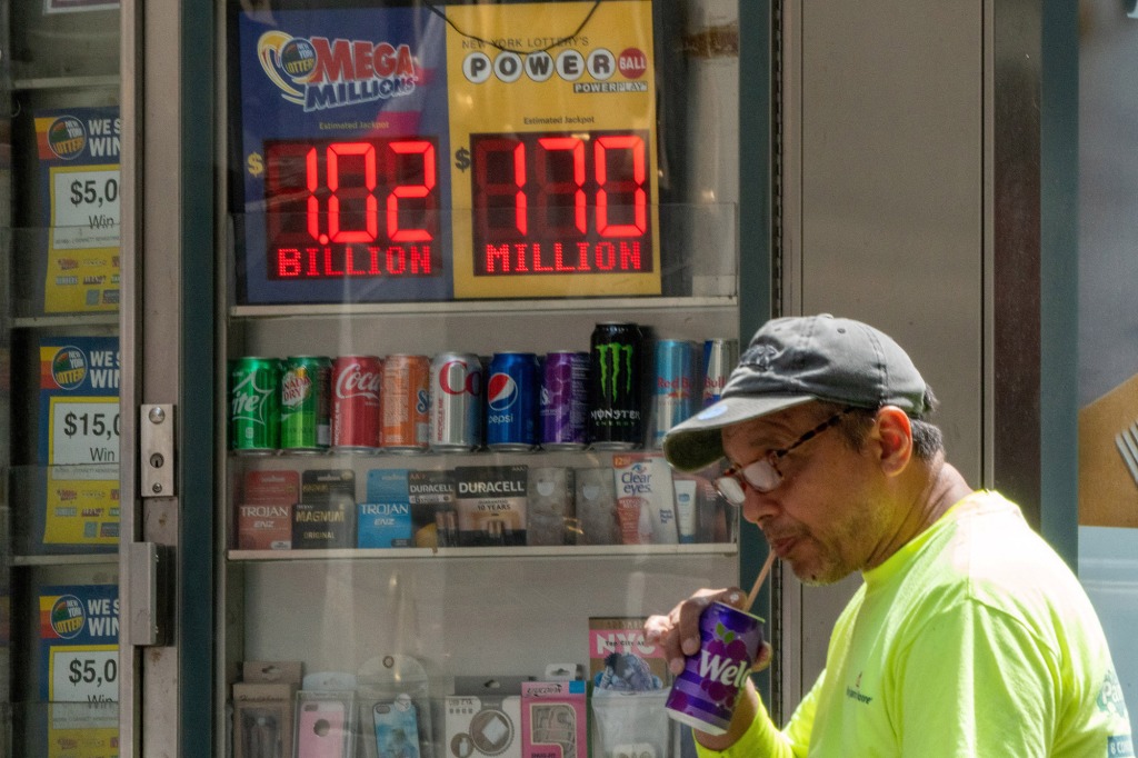 A person drinks a soda next to a digital billboard advertising the $1.2 billion Mega Millions jackpot in New York, United States, July 28, 2022.  